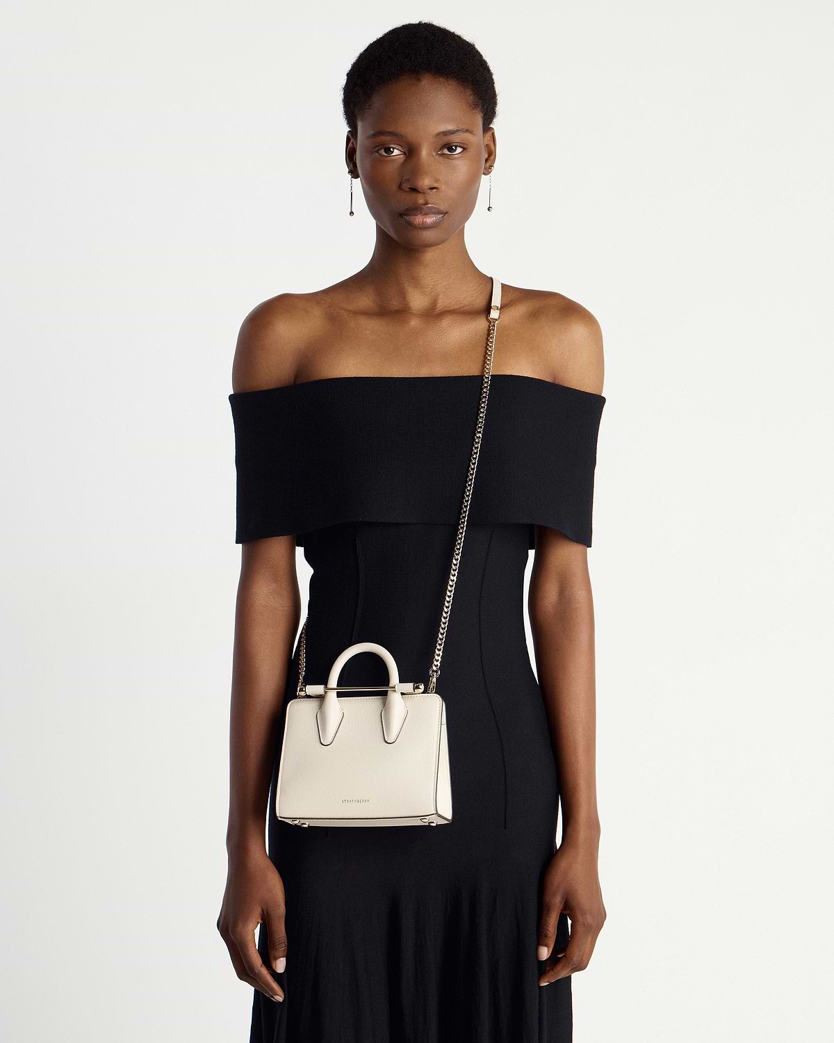 Model wearing vanilla Strathberry nano tote with chain strap and top handles.