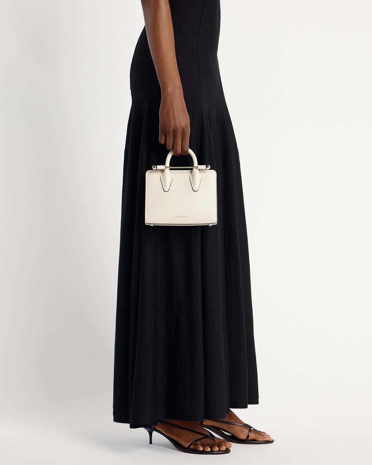 Woman holding vanilla nano tote by top handle, wearing black maxi dress.