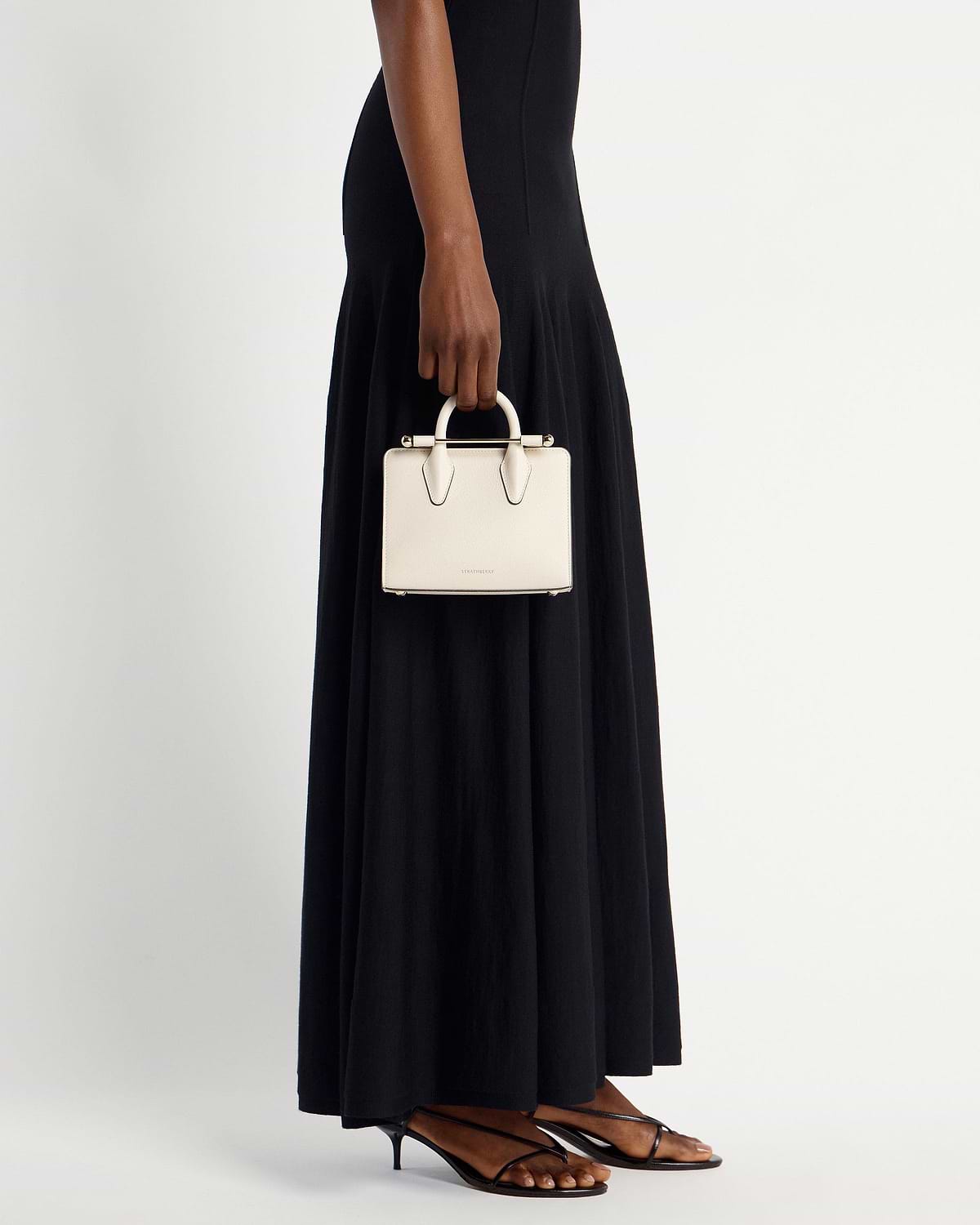 Woman holding vanilla nano tote by top handle, wearing black maxi dress.