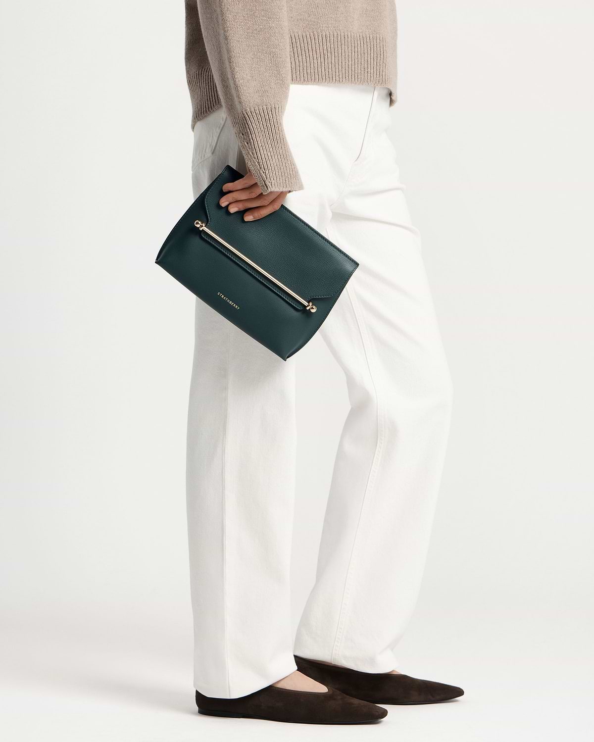 Model holding bottle green Strathberry Stylist clutch with gold bar detail.