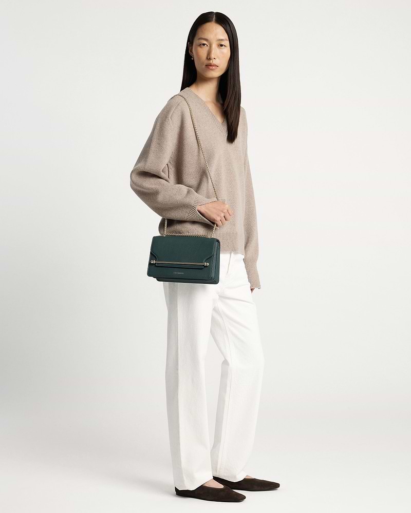 Woman wearing beige jumper and white trousers carrying bottle green east/west bag.