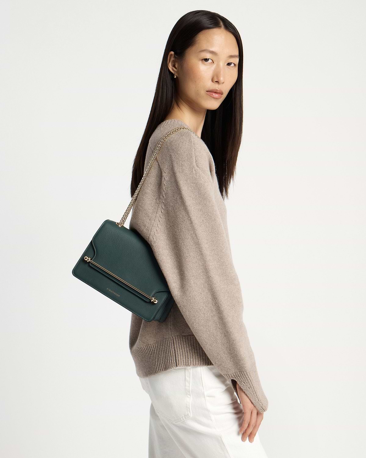 Model wearing bottle green east/west shoulder bag with gold chain strap.