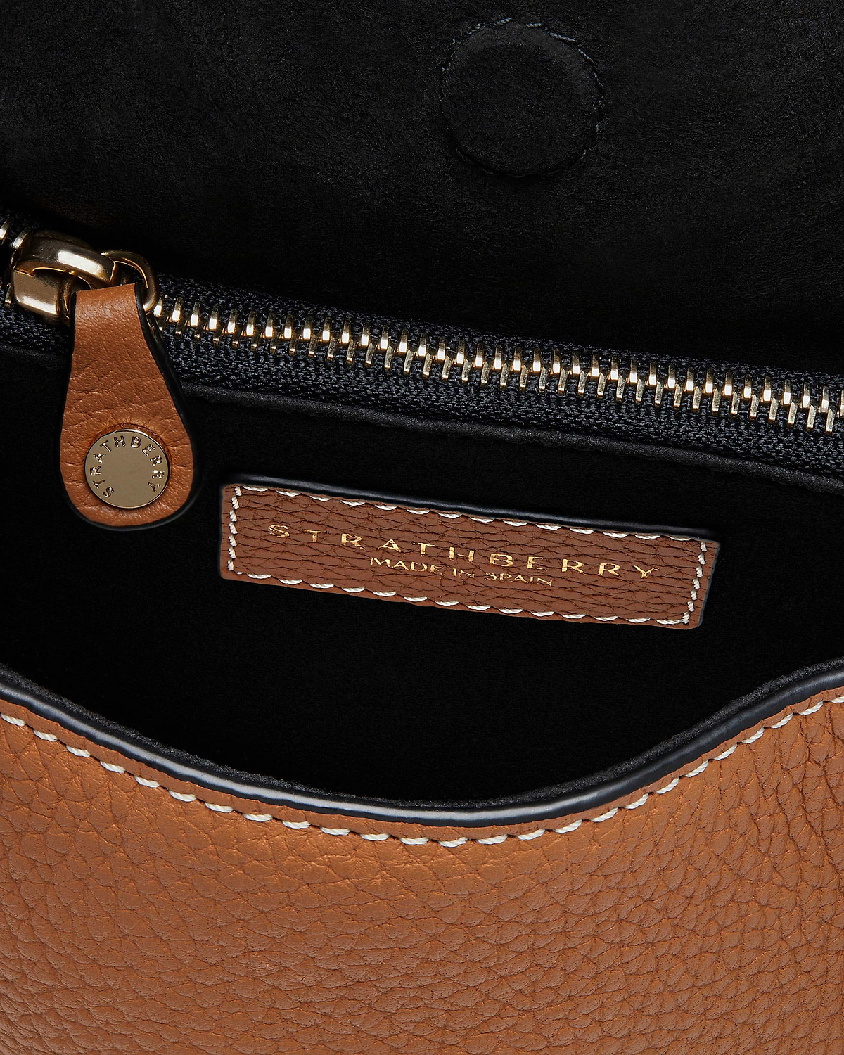 Strathberry interior label with gold zip, tan pebbled leather and vanilla stitching.