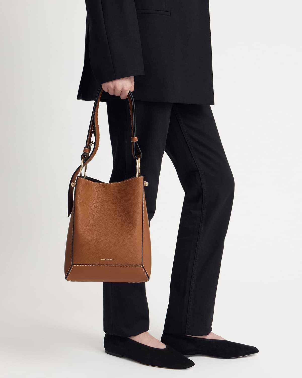 Model's lower body holding a Strathberry tan leather midi bucket bag with vanilla stitching.