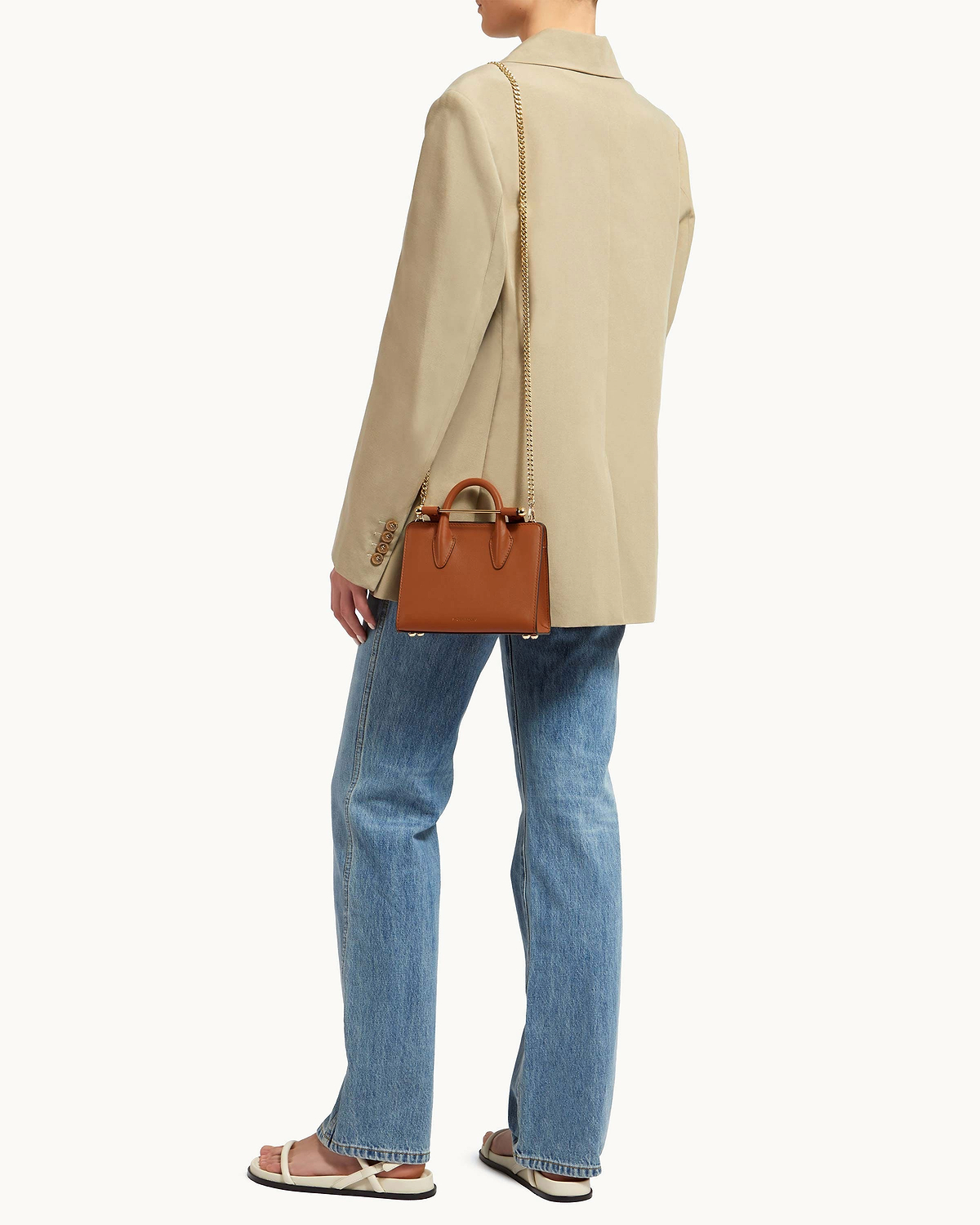 Short gold chain strap attached to small brown leather top-handle bag, worn cross-body.