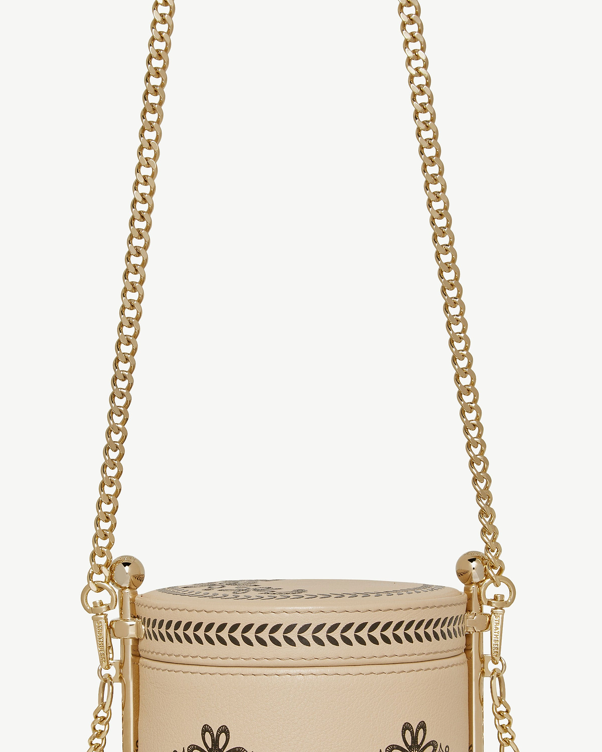 Gold short chain strap attached to beige cylindrical bag with decorative cutouts.