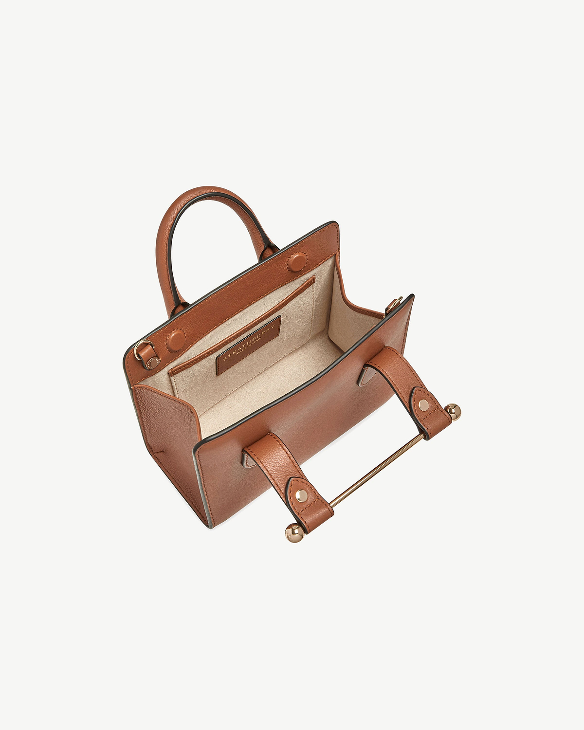 Chestnut Strathberry nano tote, open with beige interior and gold bar handle.