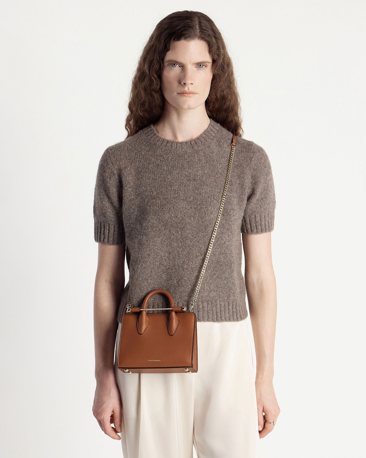Woman in brown jumper wearing chestnut Strathberry nano tote with gold chain
