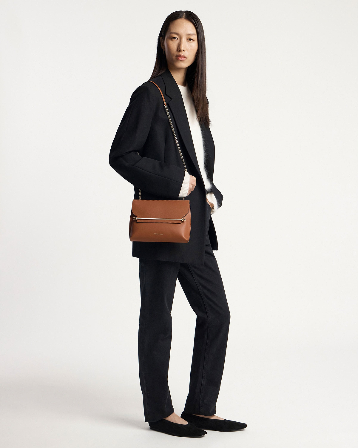 Model wearing a black blazer holding a chestnut Strathberry Stylist shoulder bag.