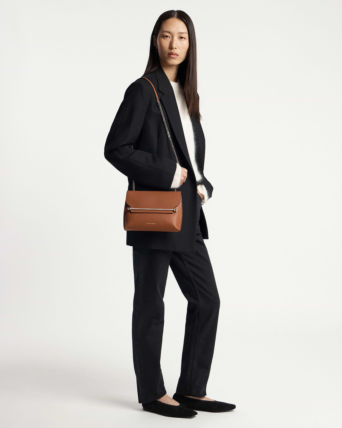Model wearing a black blazer holding a chestnut Strathberry Stylist shoulder bag.