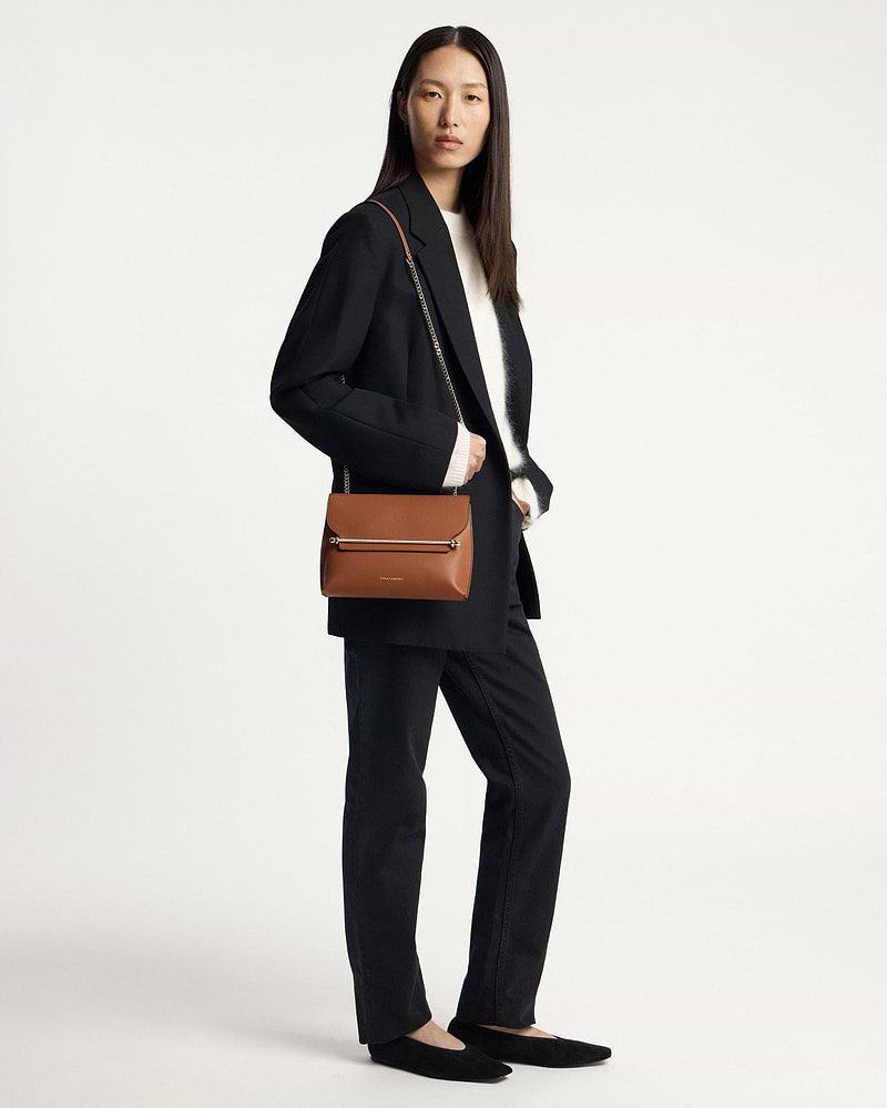 Model wearing a black blazer holding a chestnut Strathberry Stylist shoulder bag.