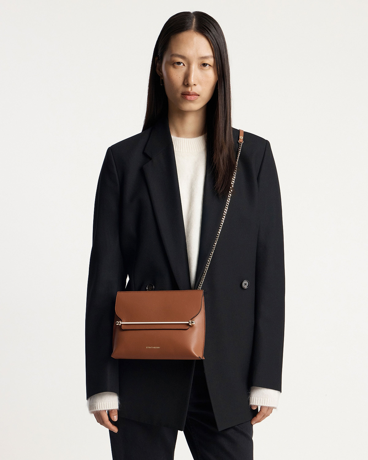 Woman wearing chestnut Stylist bag with chain strap and Strathberry logo.