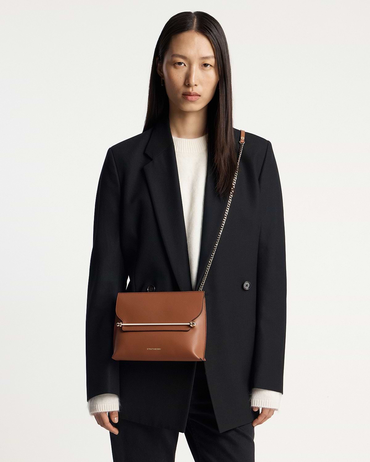 Woman wearing chestnut Stylist bag with chain strap and Strathberry logo.