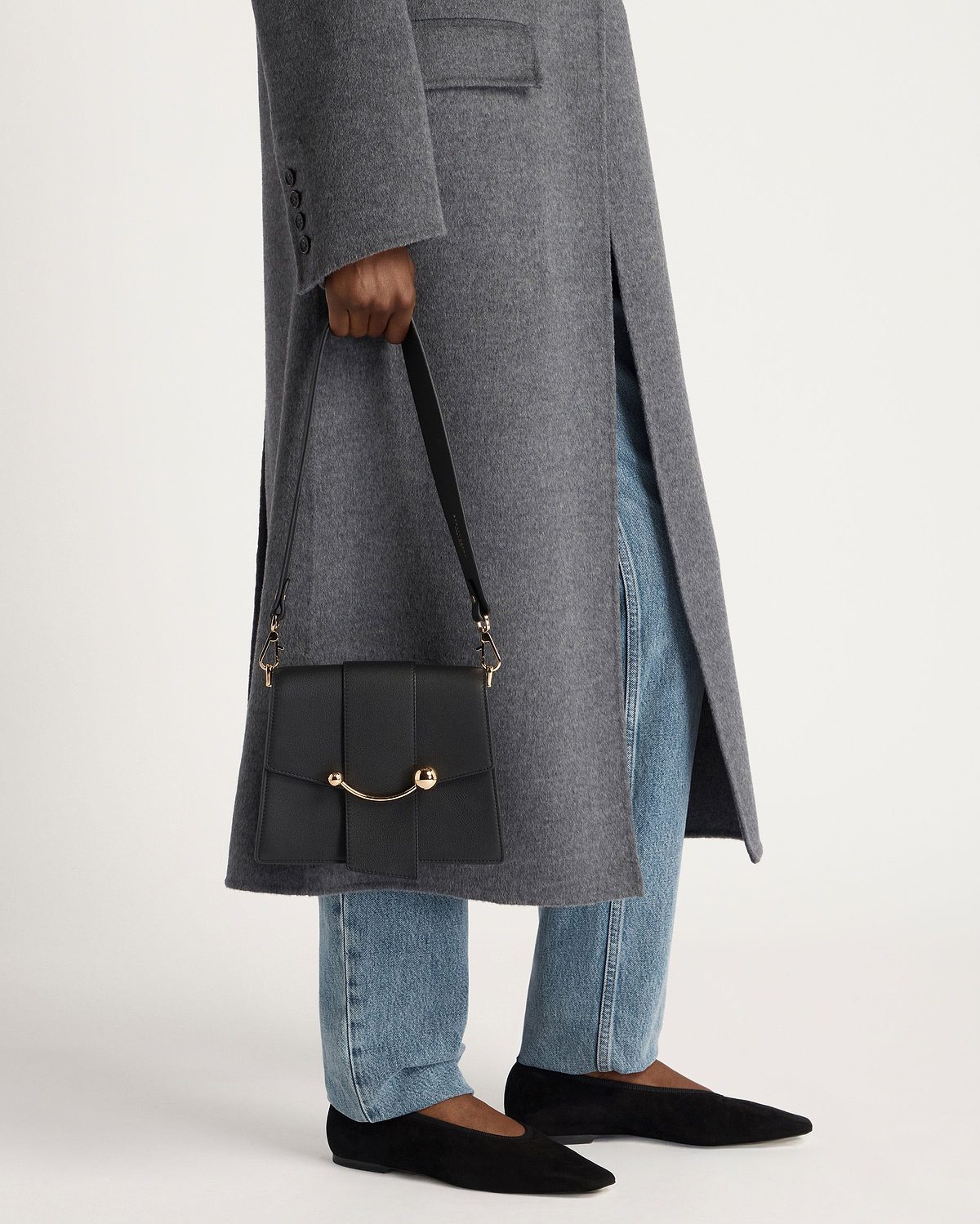 Person holding black box crescent bag with curved gold hardware, grey coat and jeans
