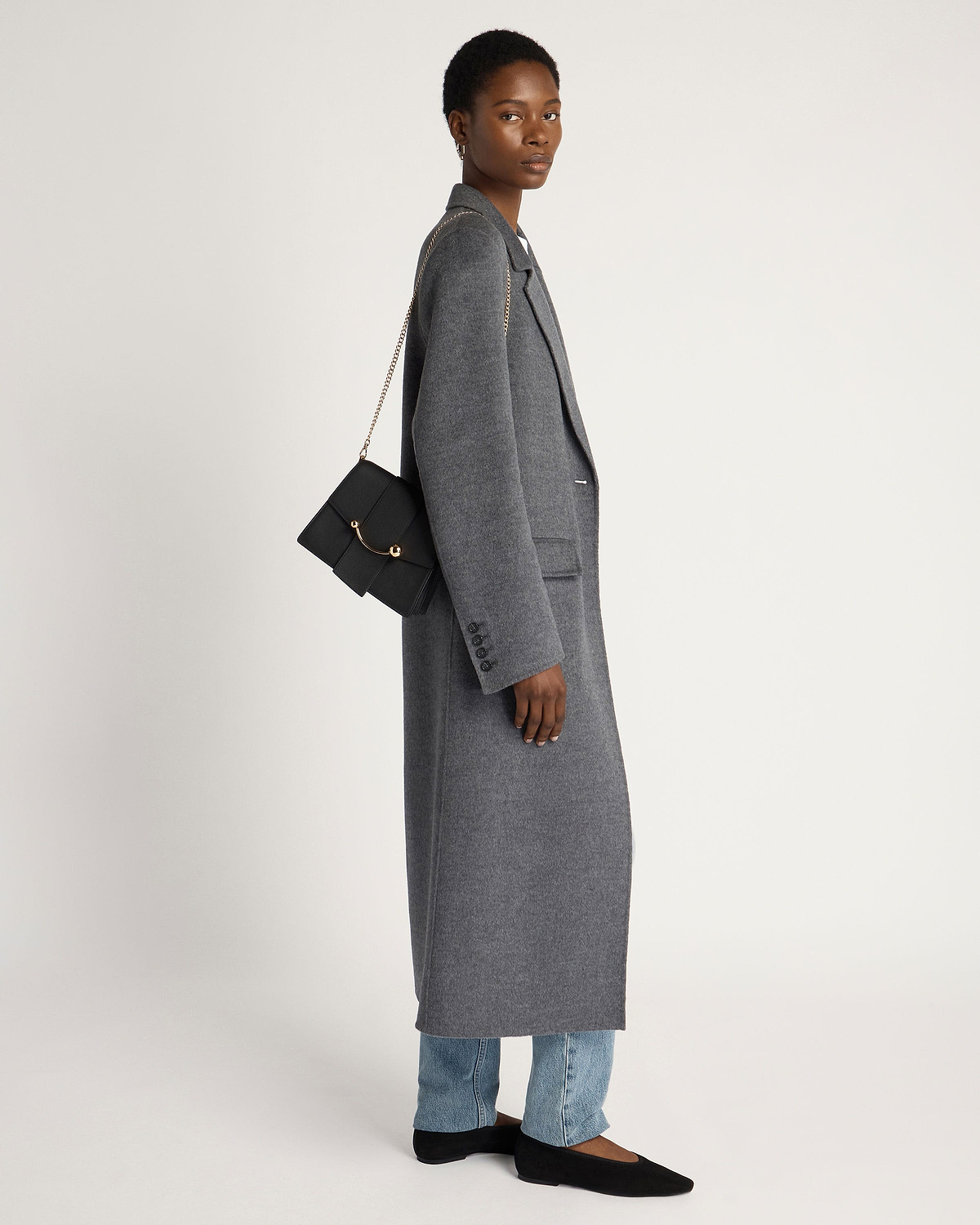 Model in grey long coat carrying black Box Crescent bag with gold chain