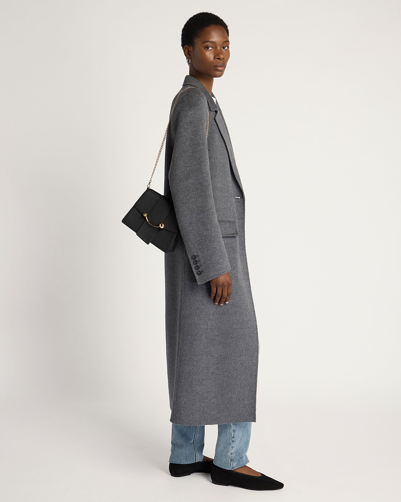Model in grey long coat carrying black Box Crescent bag with gold chain