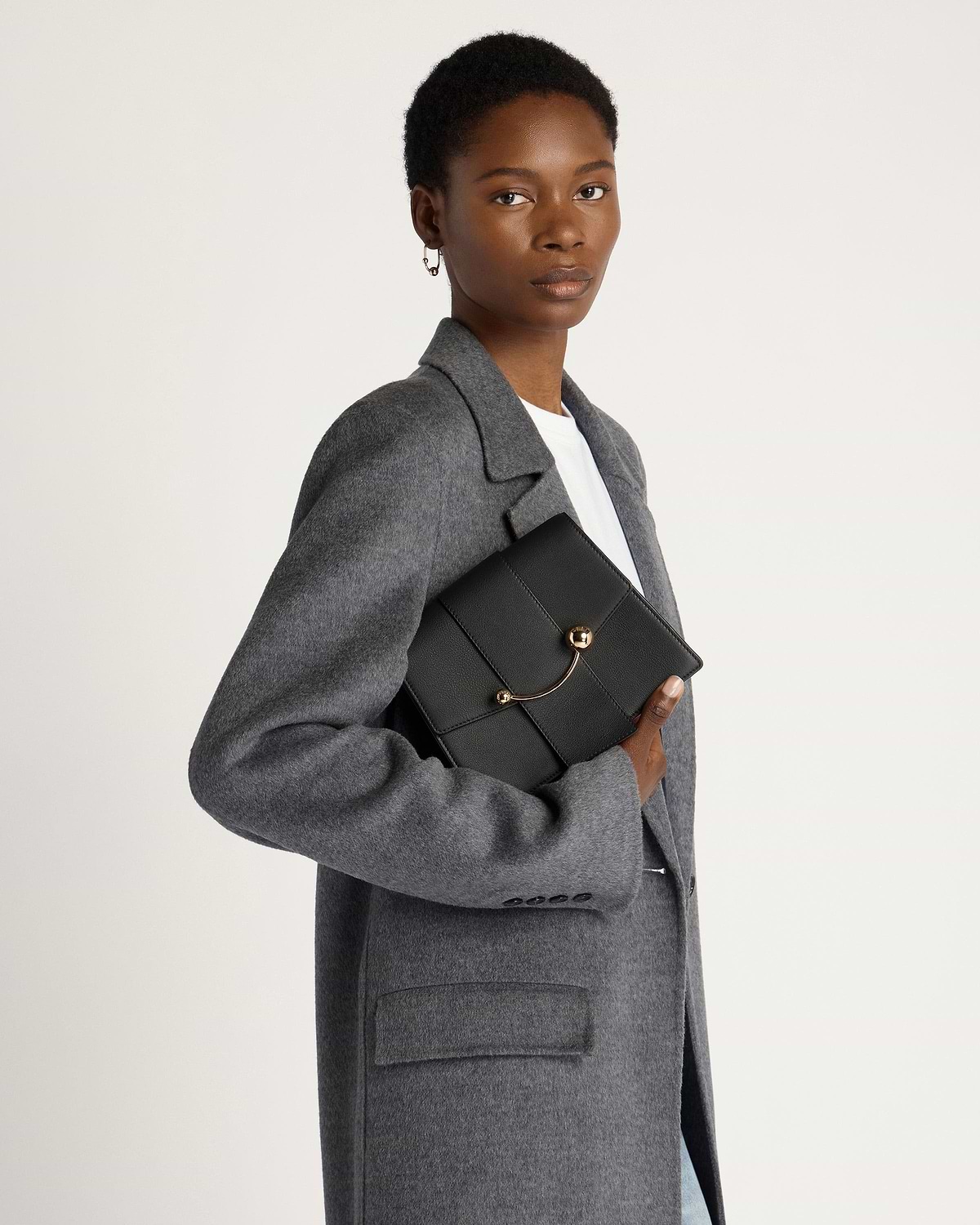 Model holding black Box Crescent bag under her arm, wearing a grey coat.