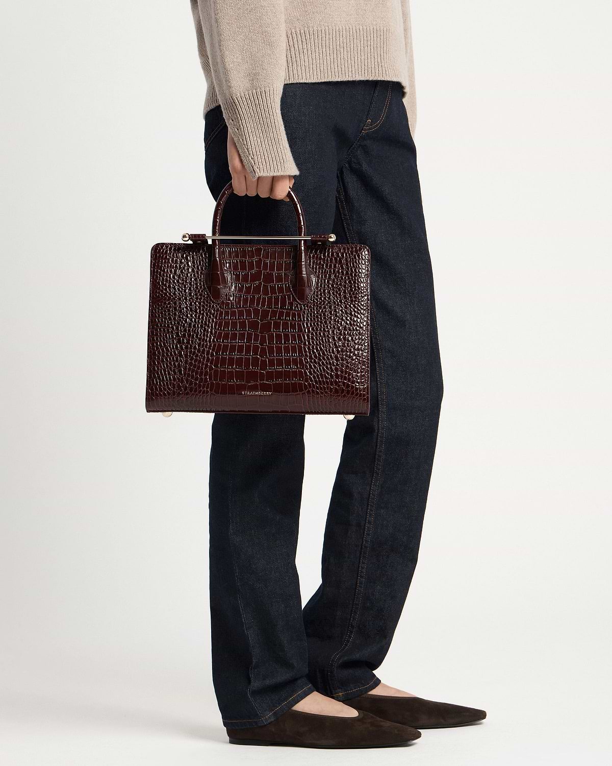 Model holding Strathberry croc-embossed midi tote in dark brown with gold hardware
