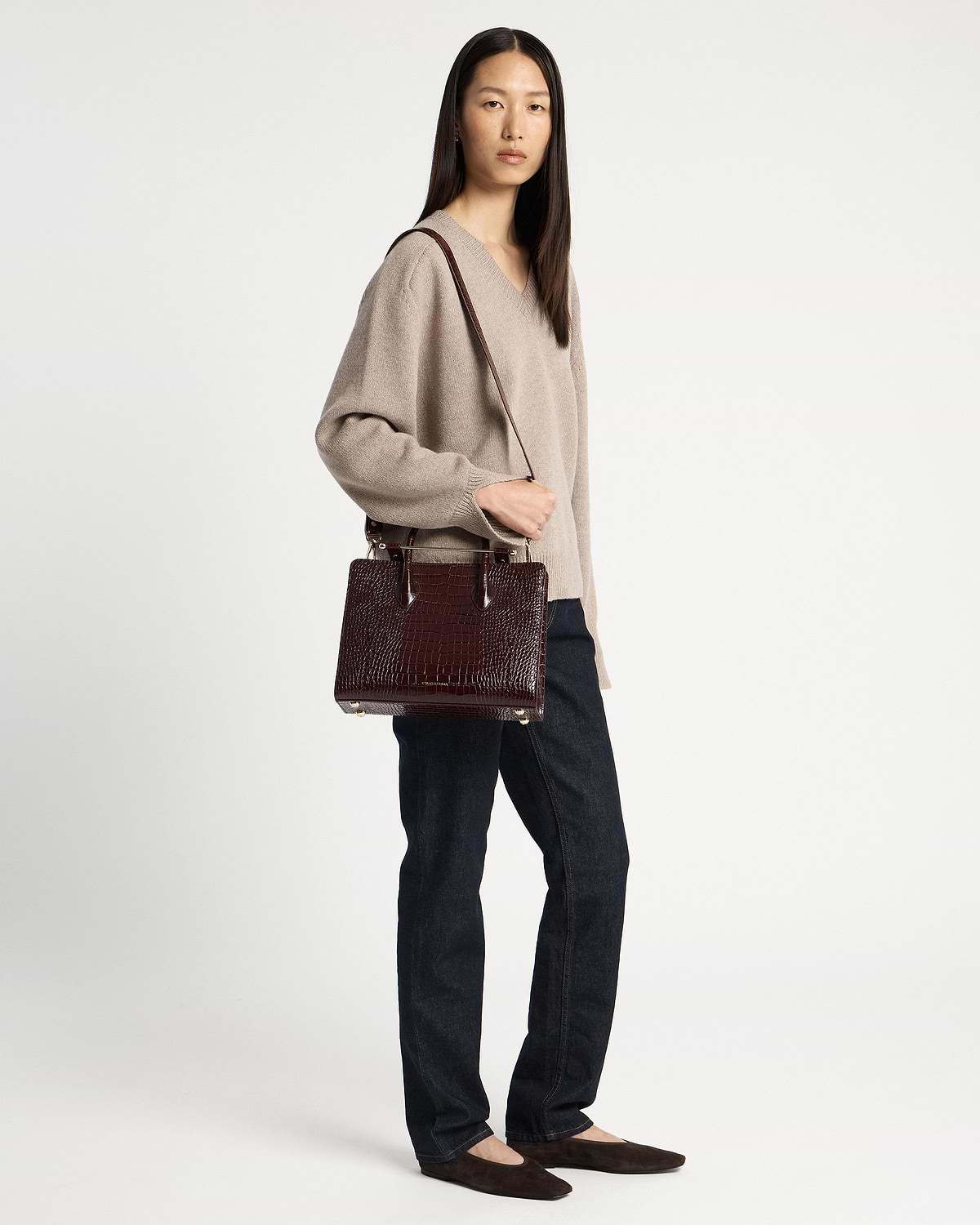 Woman wearing a beige sweater and jeans holding a croc-embossed midi tote bag.
