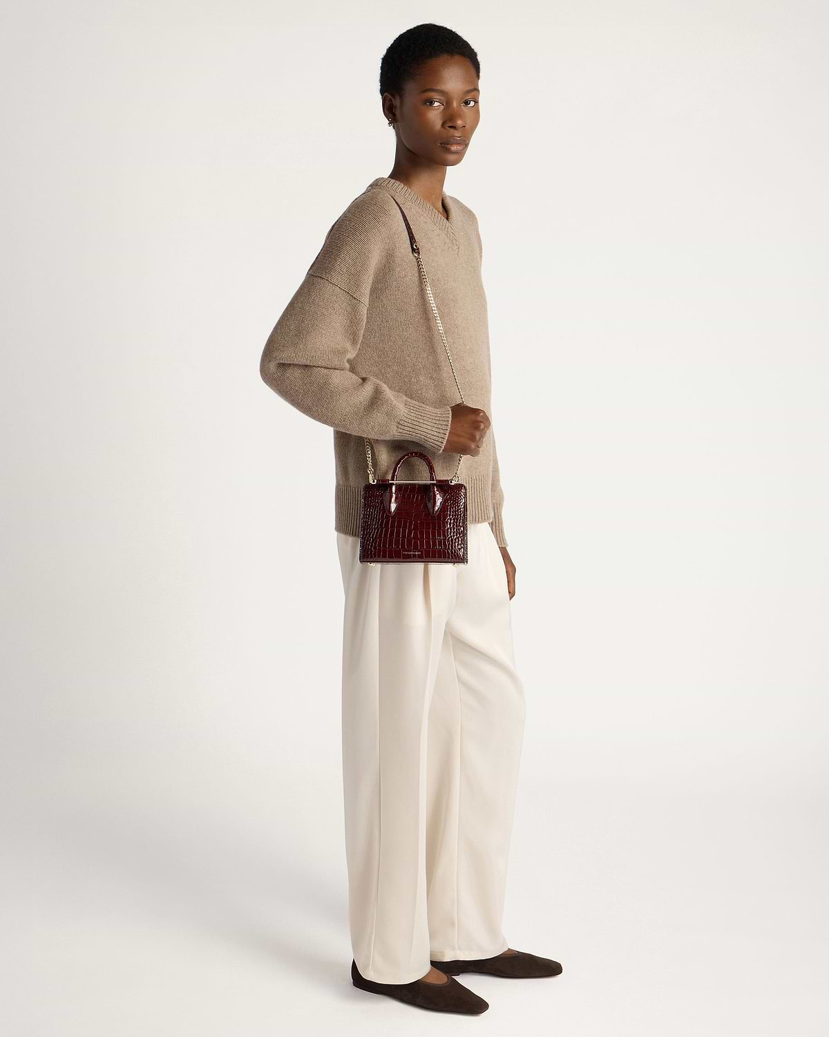 Model wearing beige jumper and cream trousers holding burgundy croc nano tote.