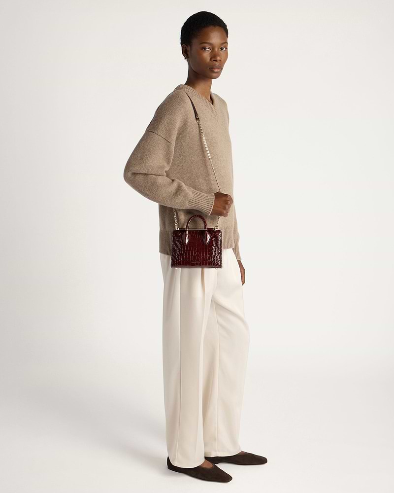 Model wearing beige jumper and cream trousers holding burgundy croc nano tote.