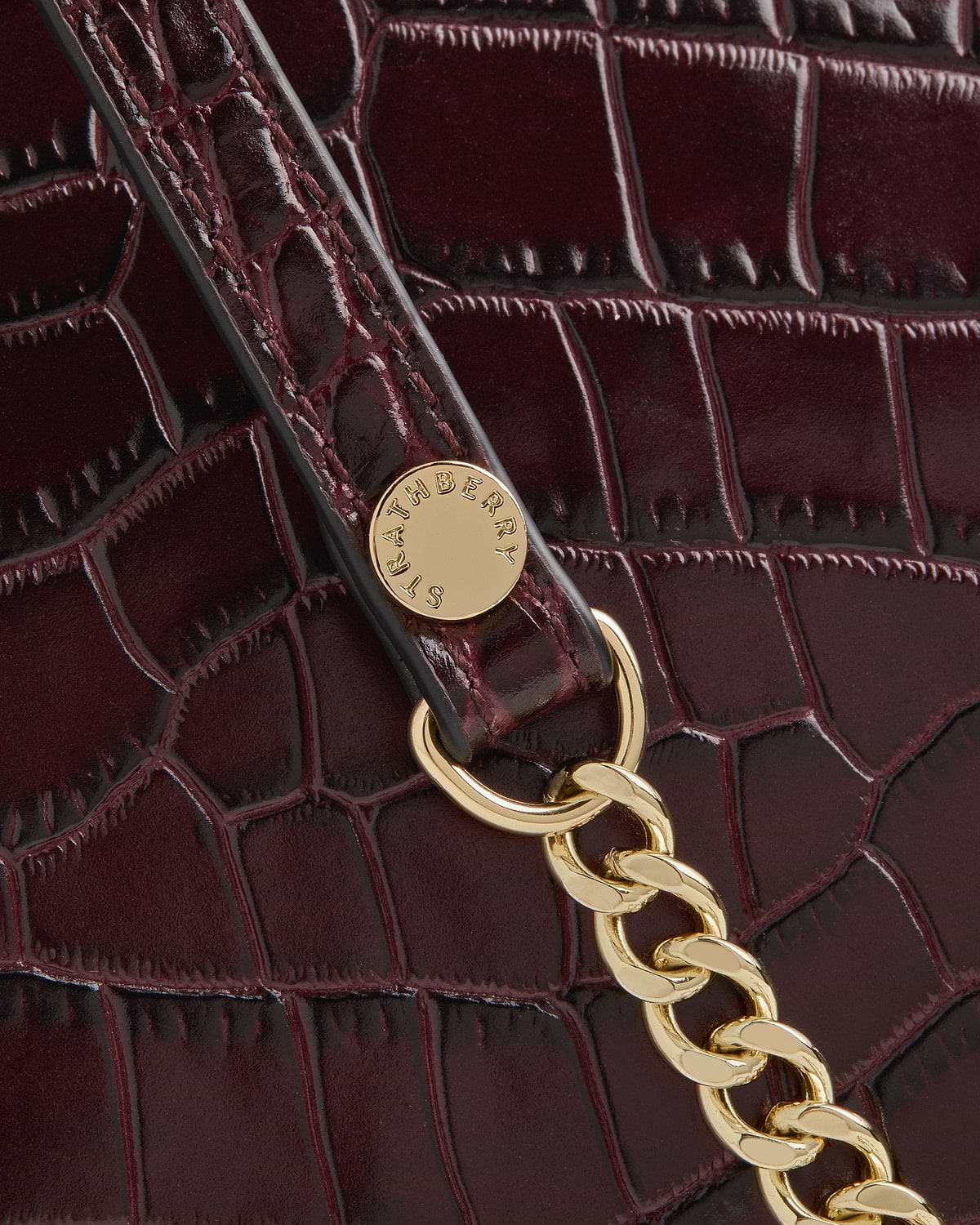 Burgundy croc-embossed leather bag detail with gold chain and Strathberry badge.