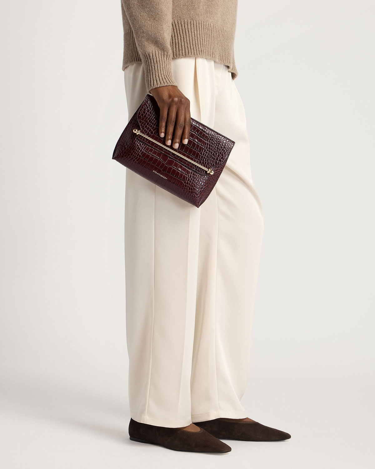 Model waist-down holding Strathberry croc-embossed Stylist leather clutch in burgundy.
