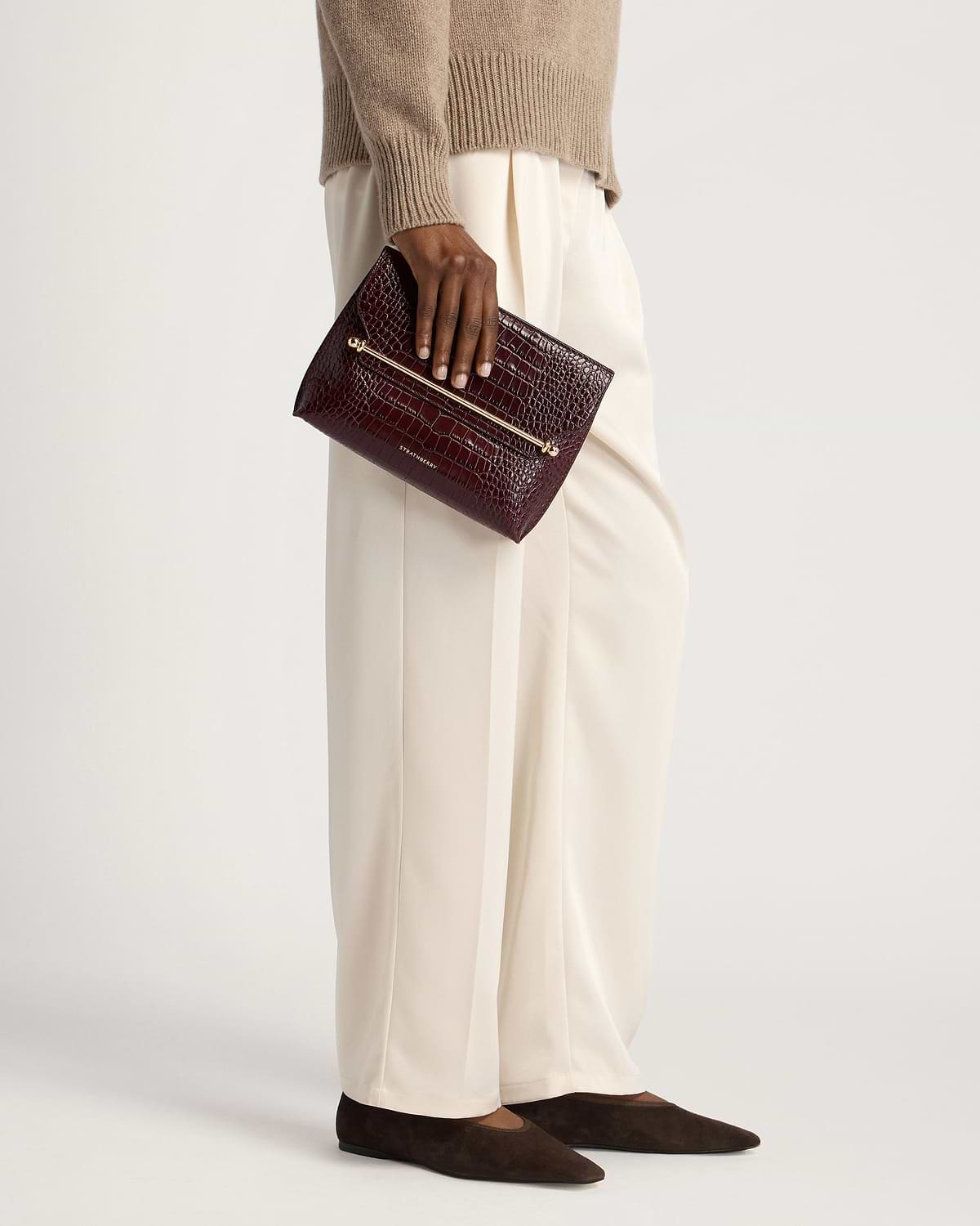 Model waist-down holding Strathberry croc-embossed Stylist leather clutch in burgundy.
