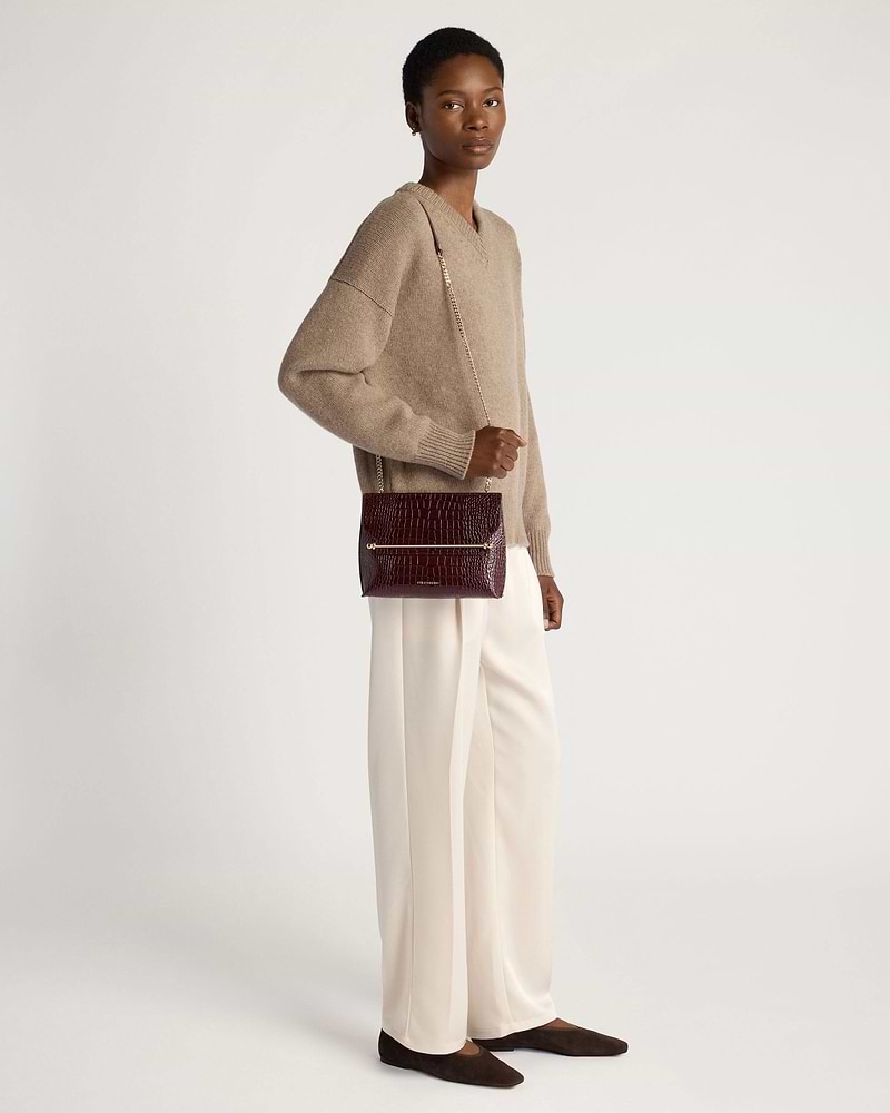 Model wearing croc-embossed burgundy crossbody bag with gold chain strap.