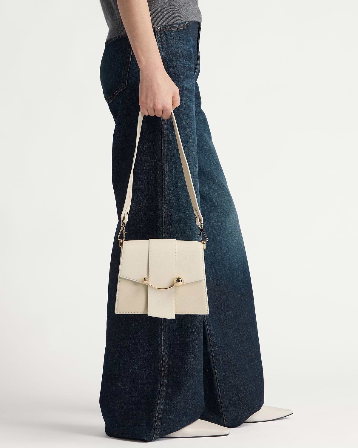 Model holding vanilla box handbag with gold crescent bar and strap.