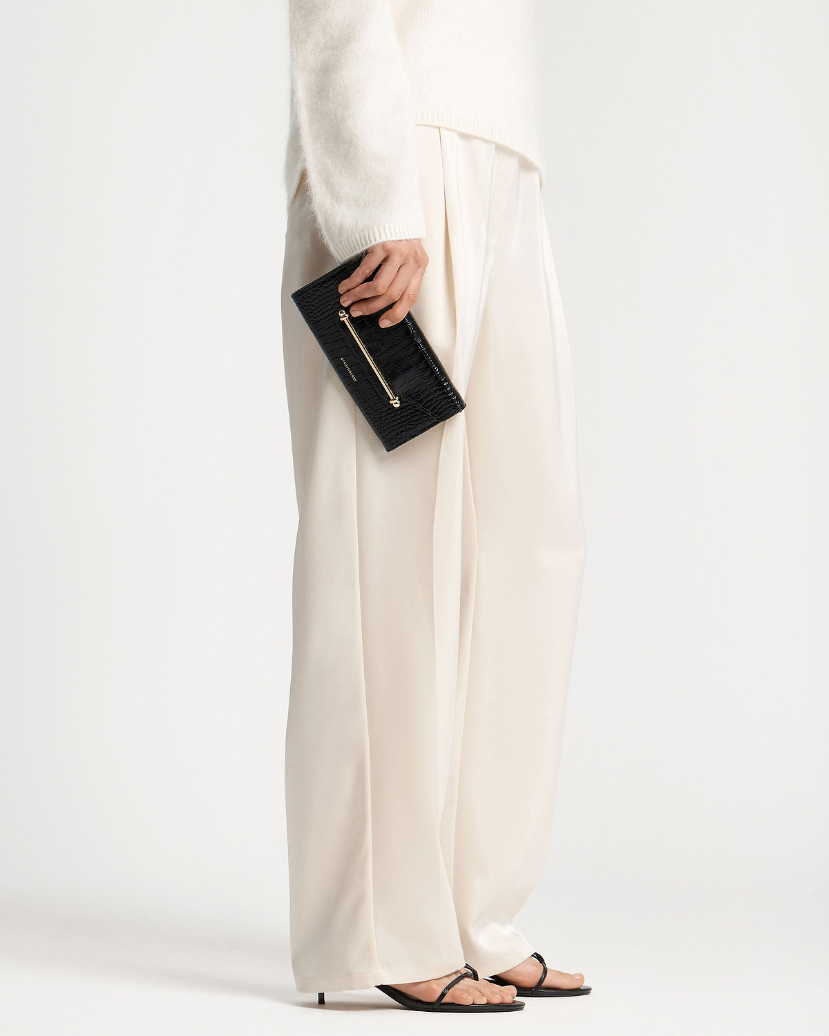 Hand holding black croc-effect textured wallet with gold bar detail