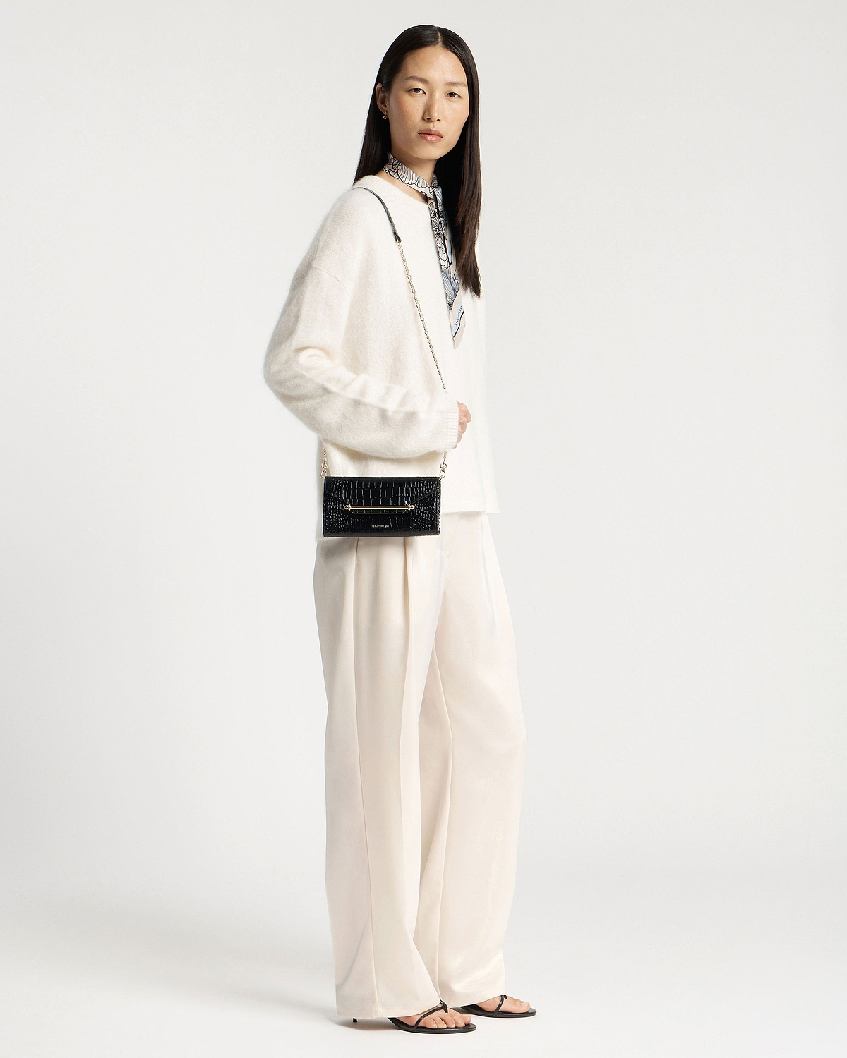 Model wearing a black crocodile-effect chain wallet with a gold chain strap.