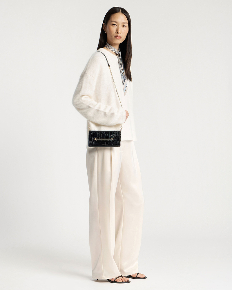 Model wearing a black crocodile-effect chain wallet with a gold chain strap.