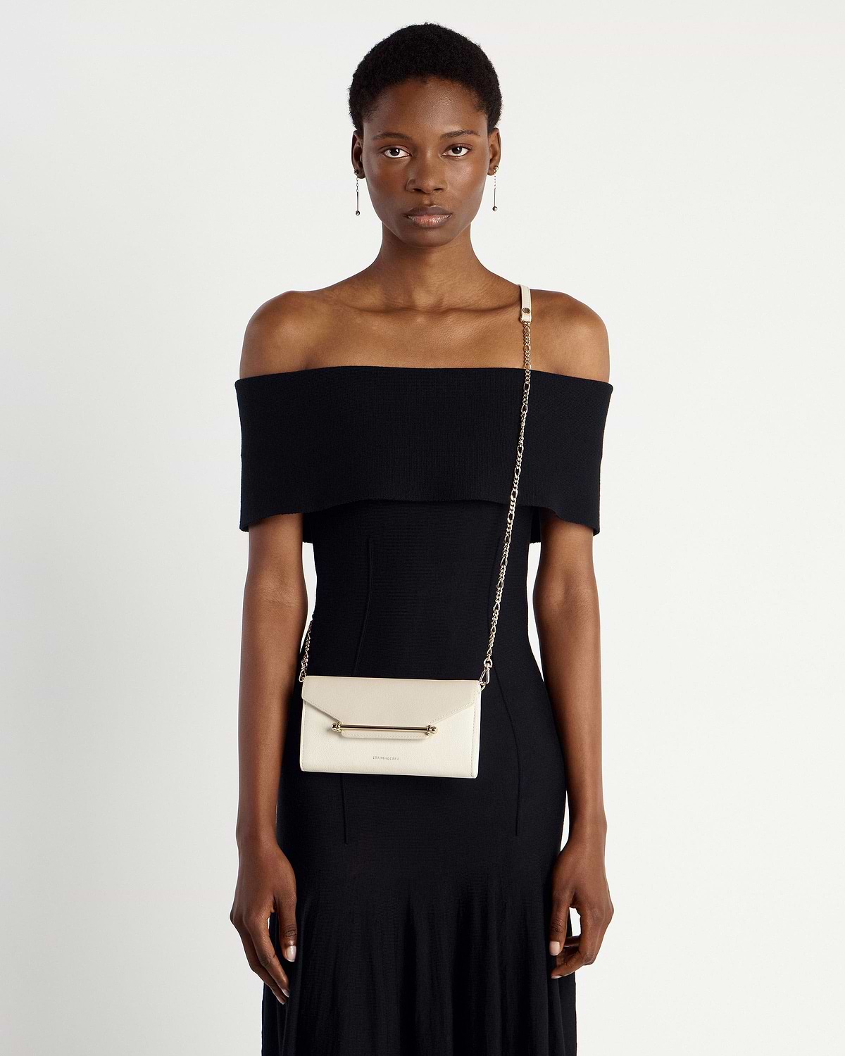 Model wearing black off-shoulder dress with Strathberry Multrees chain wallet in vanilla diamond.