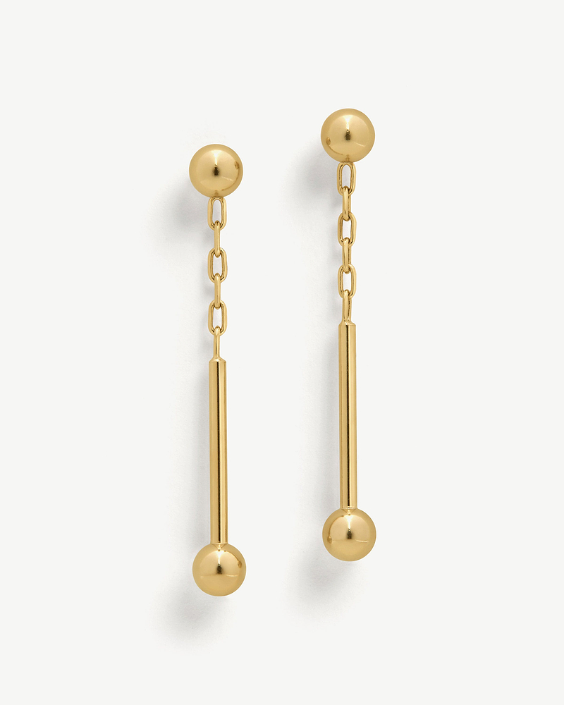 Pair of 22 carat gold gilded music bar drop earrings on a white background.