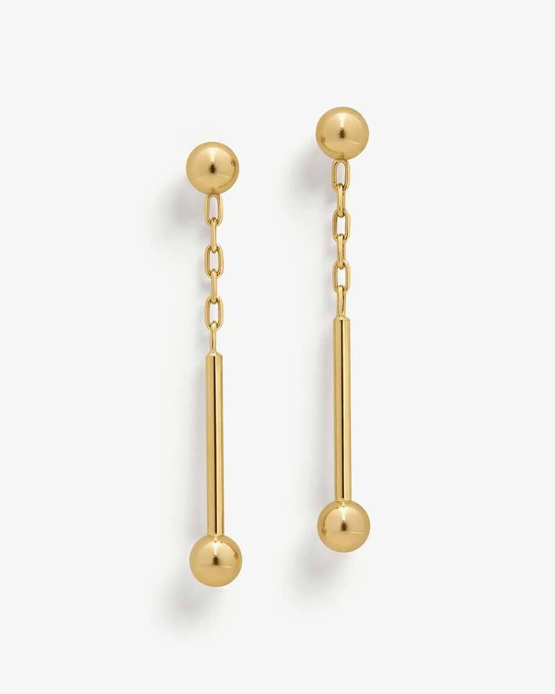 Pair of 22 carat gold gilded music bar drop earrings on a white background.