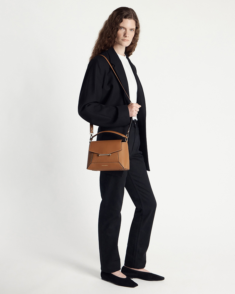 Model wearing black blazer carrying tan mosaic bag with vanilla stitching over shoulder.