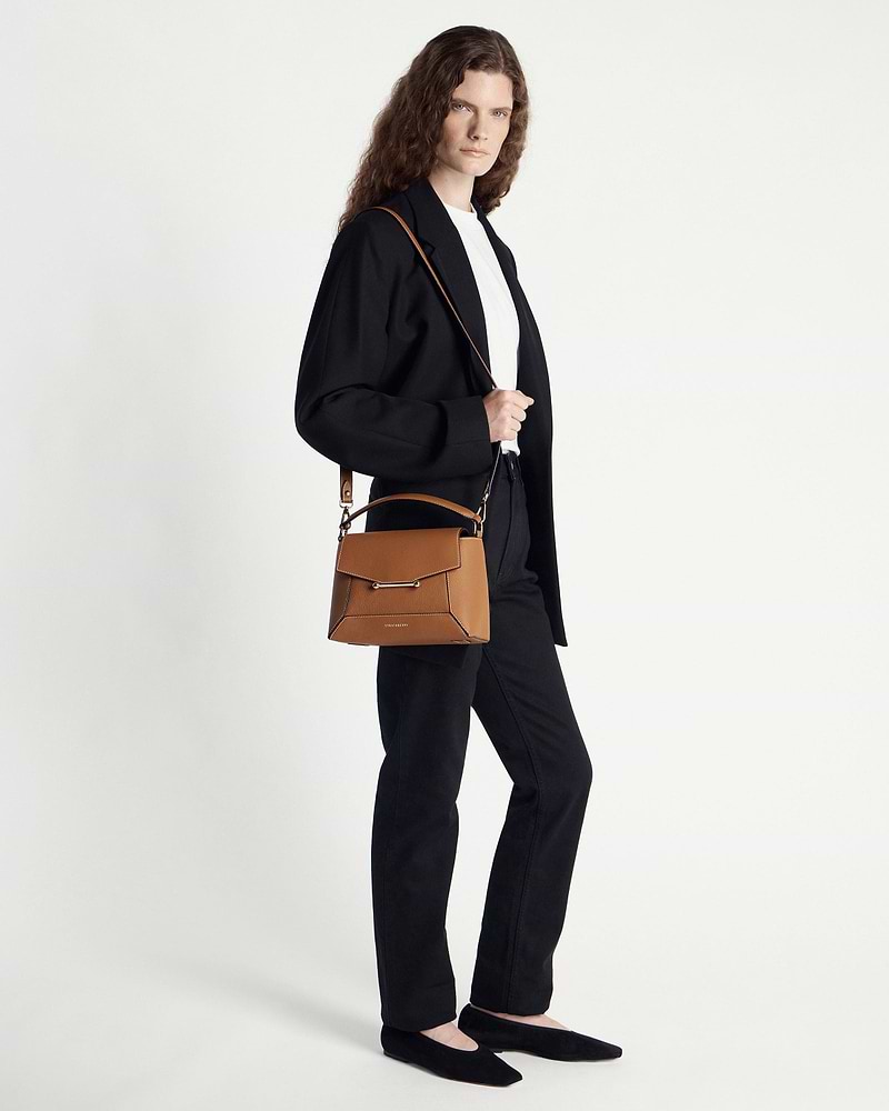 Model wearing black blazer carrying tan mosaic bag with vanilla stitching over shoulder.