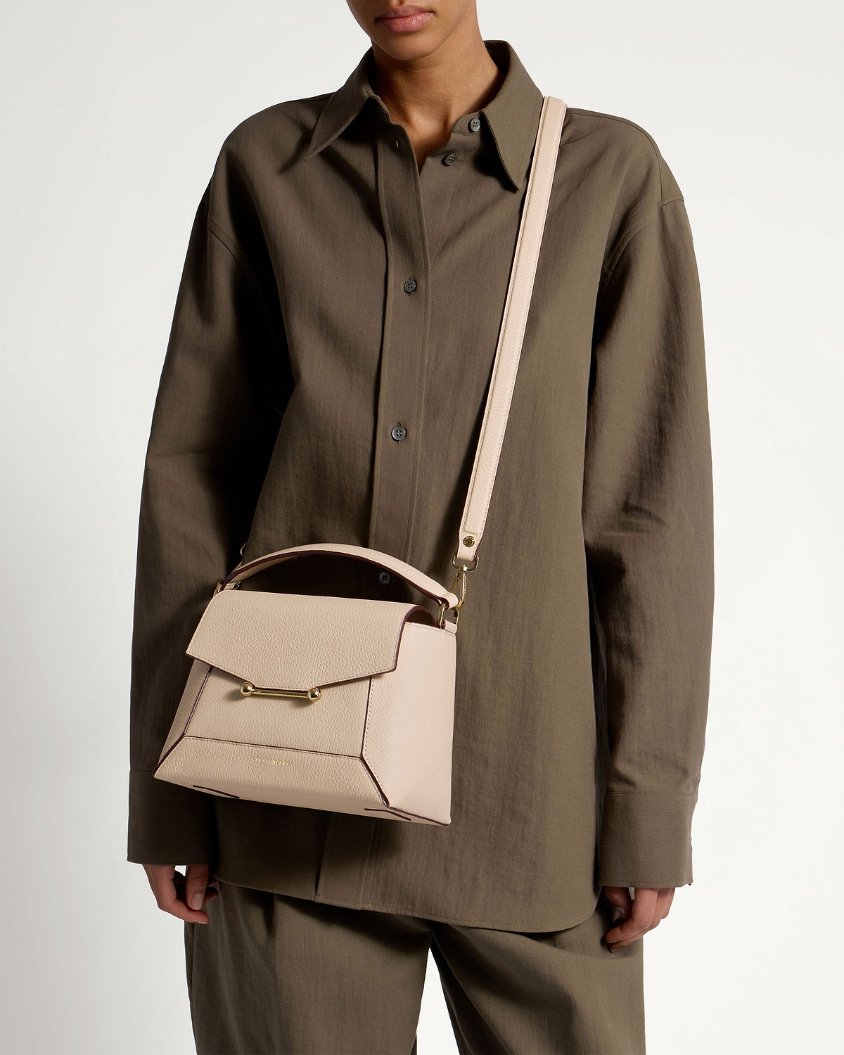 Model wearing oat mosaic bag crossbody with top handle and gold bar hardware.