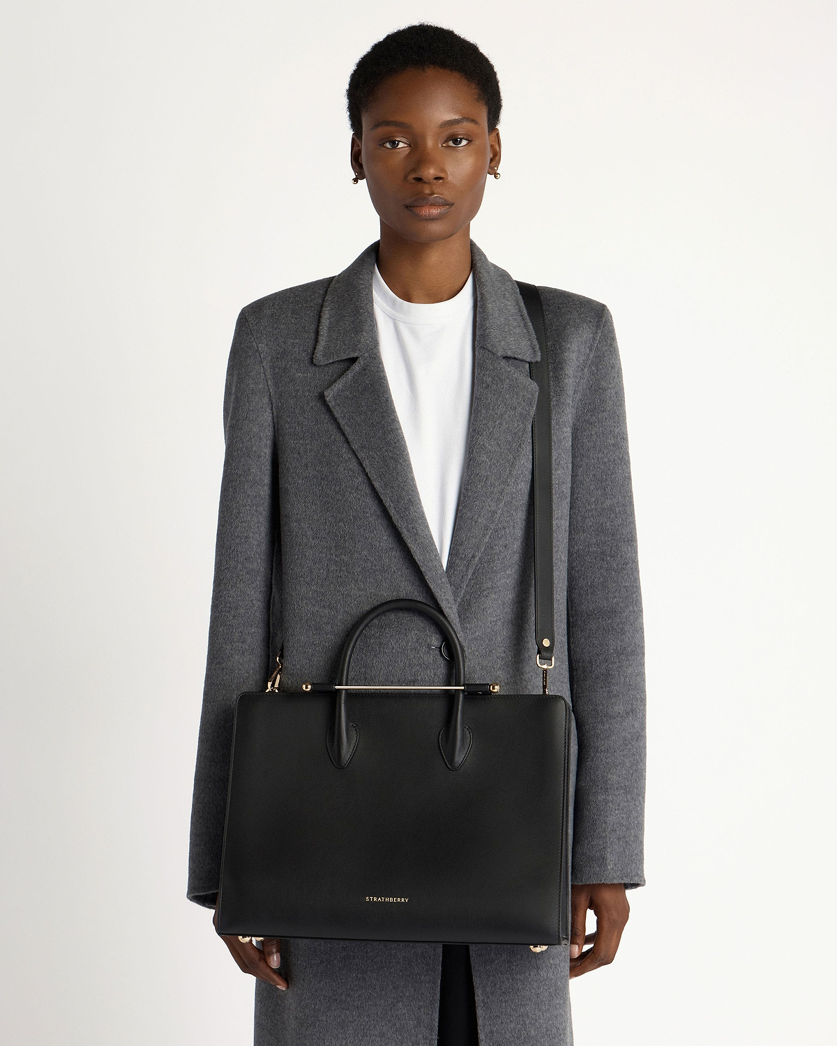 Model wearing grey coat with black Strathberry leather tote and gold hardware.