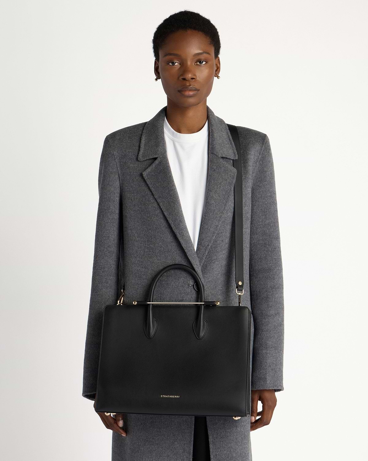 Model wearing grey coat with black Strathberry leather tote and gold hardware.