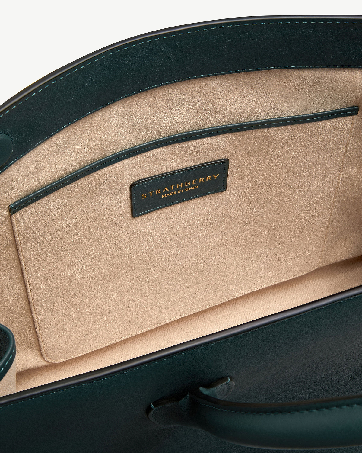 Bottle green leather tote interior showing beige suede lining, pocket and Strathberry label.