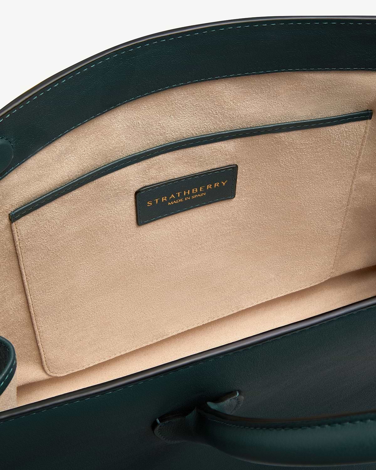 Bottle green leather tote interior showing beige suede lining, pocket and Strathberry label.
