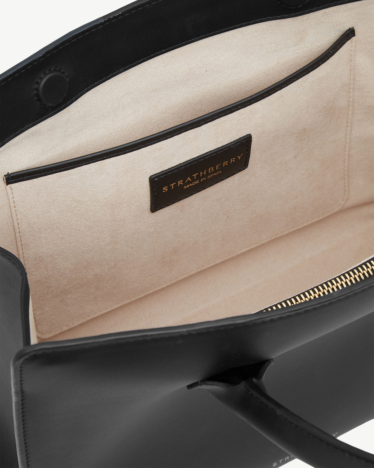 Interior of black midi tote showing beige lining, pocket, gold zip, Strathberry label.