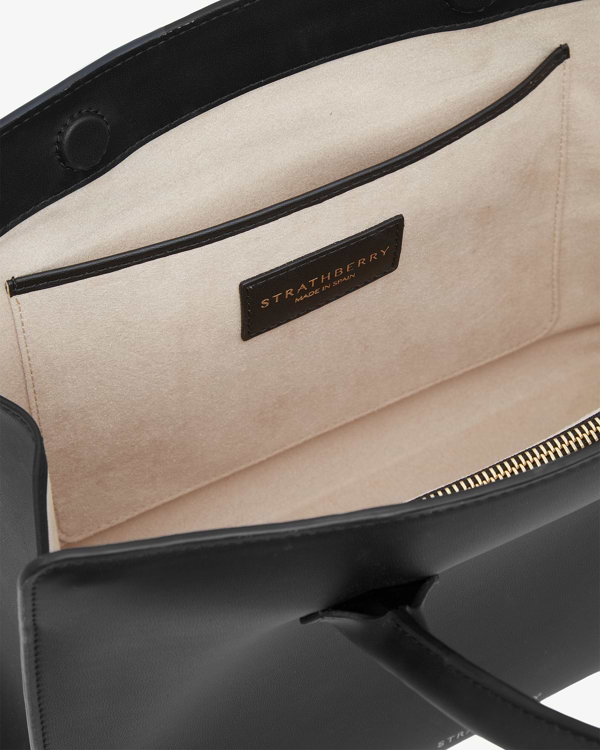 Interior of black midi tote showing beige lining, pocket, gold zip, Strathberry label.