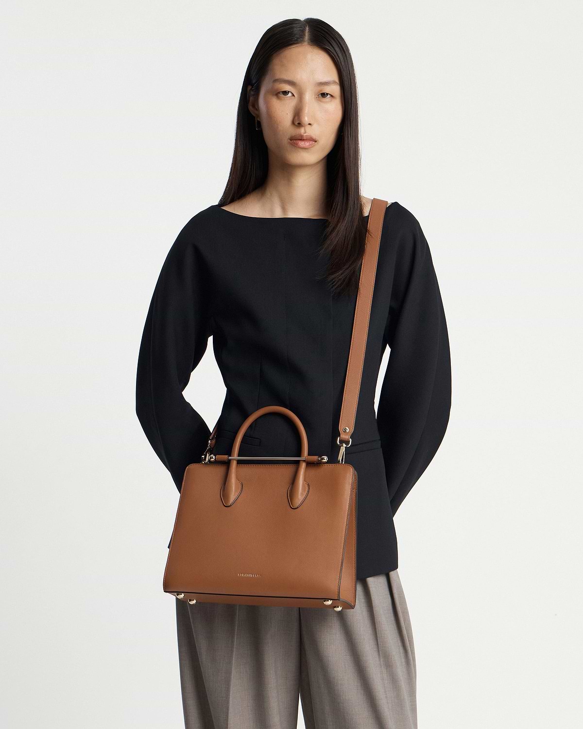 Model wearing Strathberry chestnut midi tote with top handles and shoulder strap.