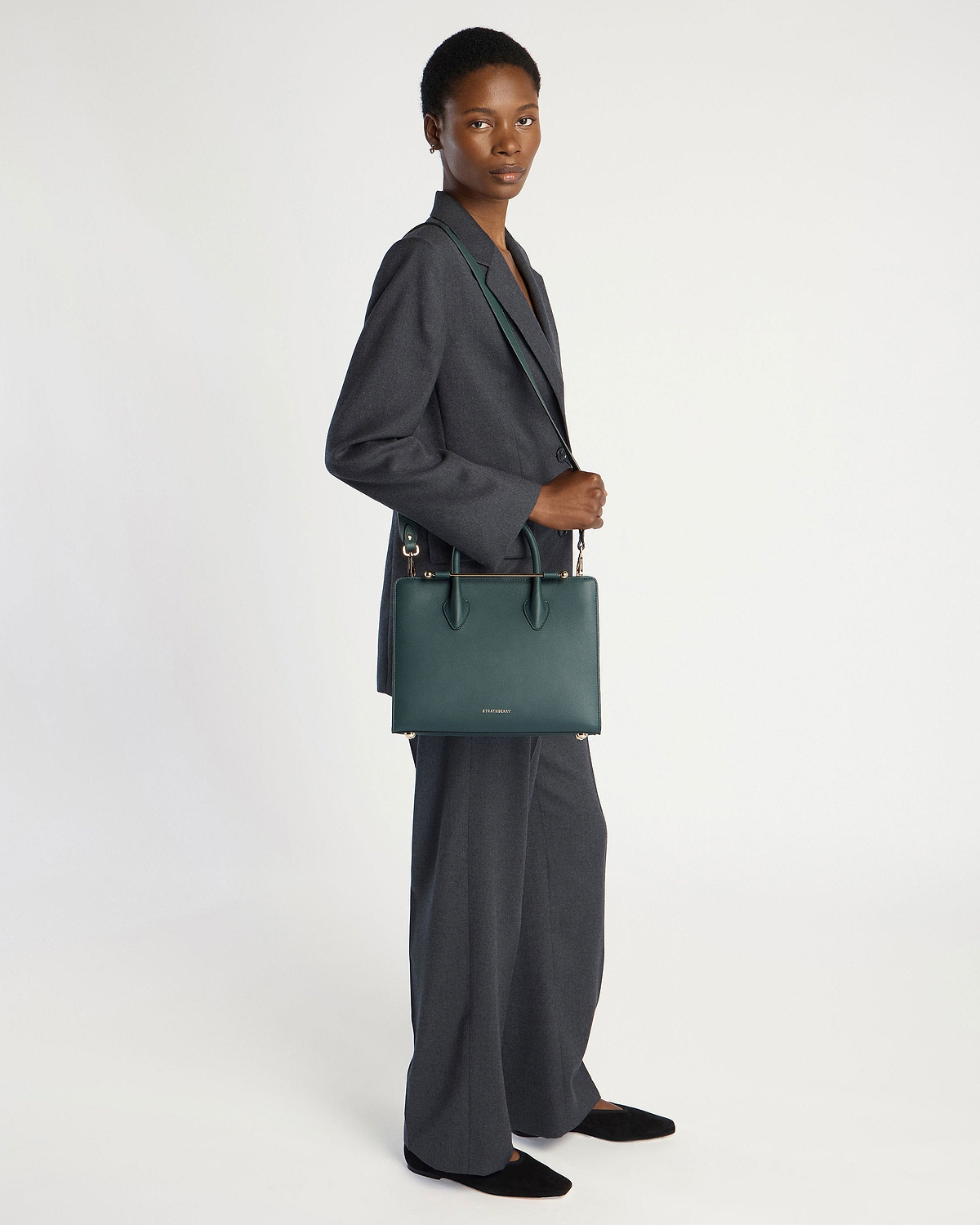 Model wearing a grey suit carrying a bottle green midi tote bag.