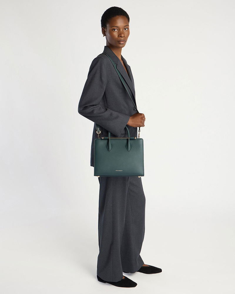 Model wearing a grey suit carrying a bottle green midi tote bag.