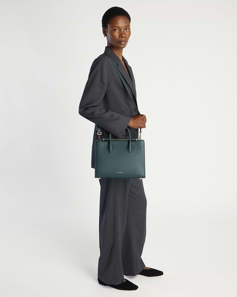 Model wearing a grey suit carrying a bottle green midi tote bag.