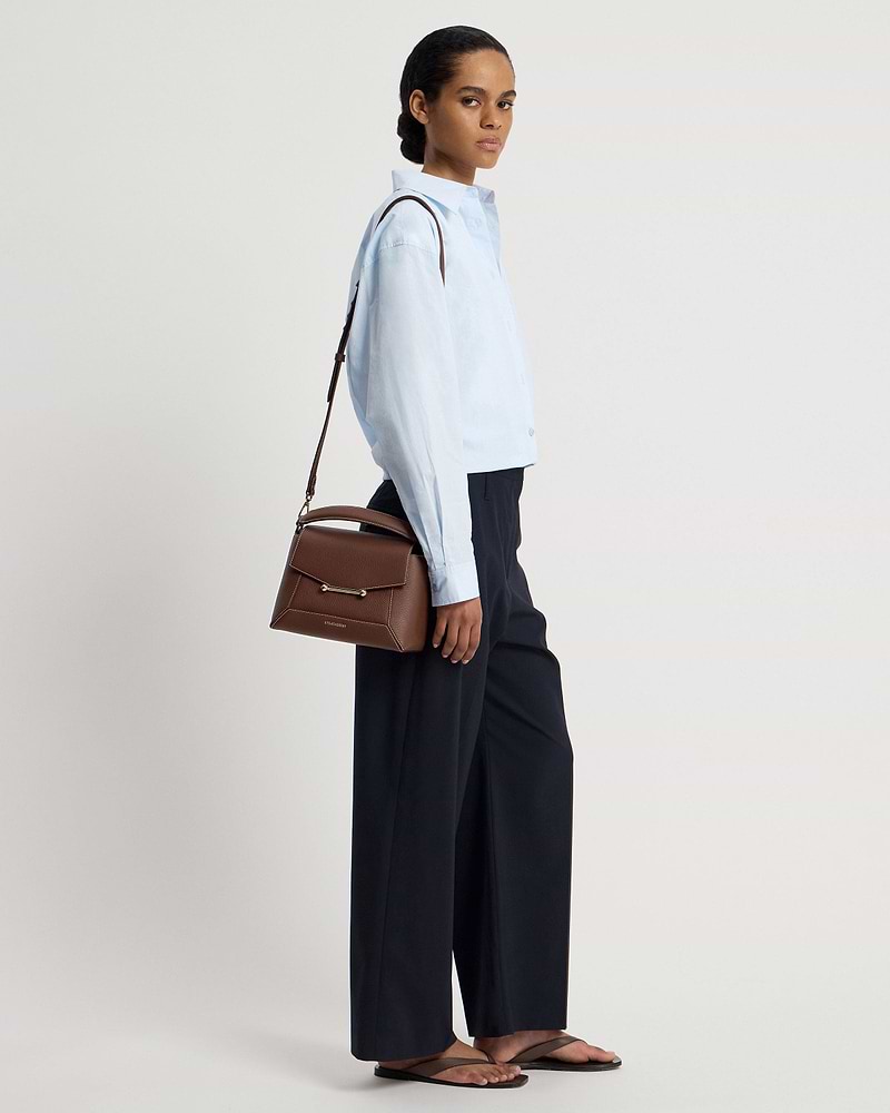 Model wearing a light blue shirt carrying a chocolate mosaic bag with vanilla stitch.